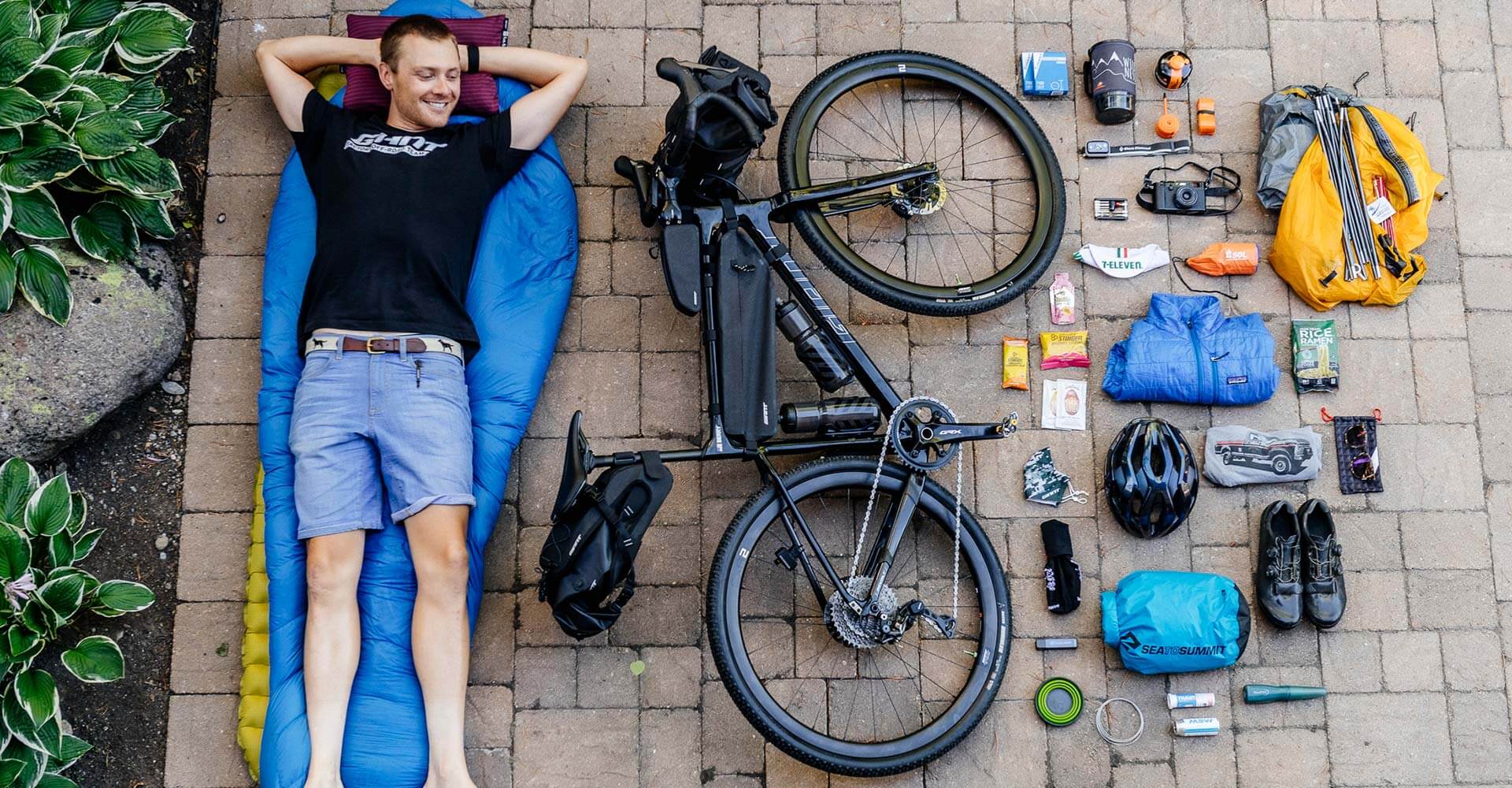 Hombre recostado junto a una bicicleta y muchos accesorios